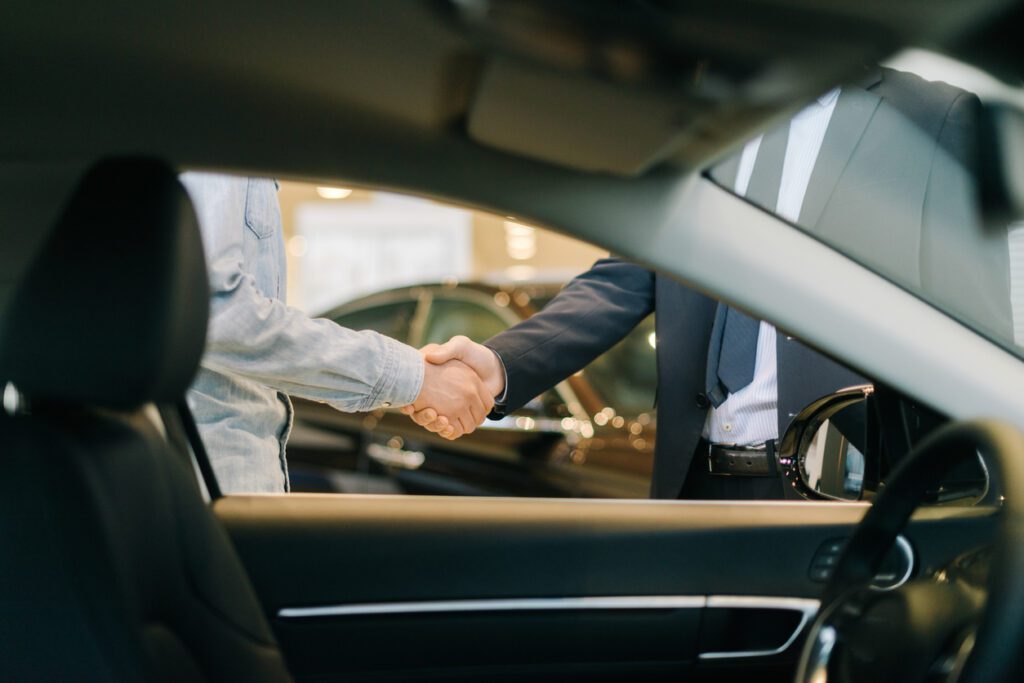 buyer-of-car-shaking-hands-with-seller-in-auto-dealership-view-from